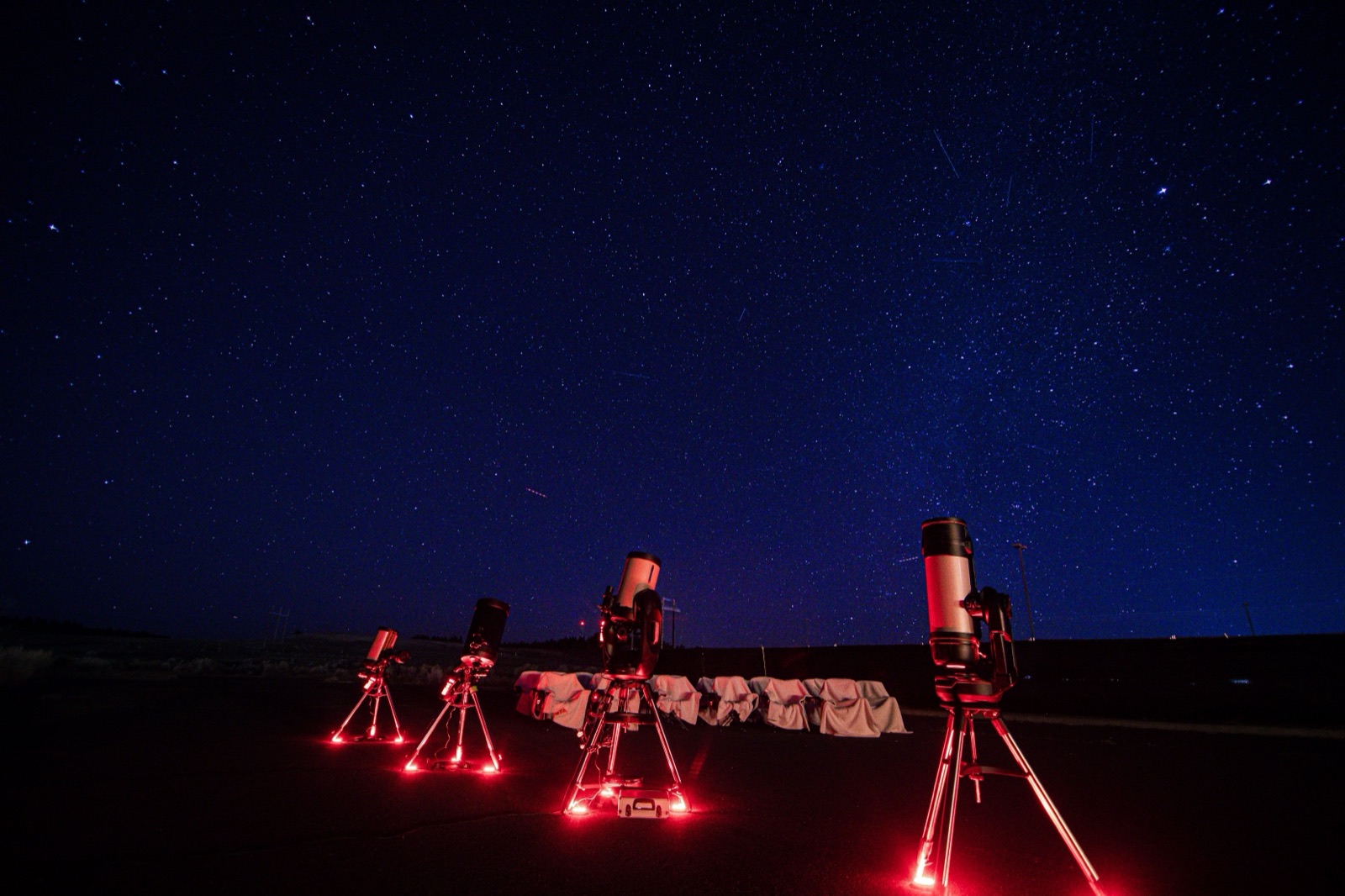 Four telescopes set up under red ground lighting beneath a deep blue starry sky on a Bryce Canyon Stargazing tour