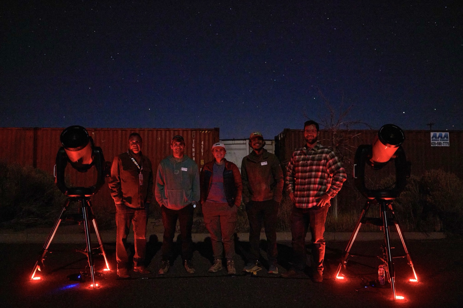 Smiling tour group gathered around telescopes after a Bryce Canyon Stargazing night tour